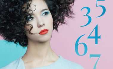 A woman with short curly hair looks at numbers for the Numerology Personal Month in October 2022.