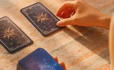 View over a person's shoulder, showing their hand and two Tarot cards on a table.