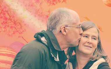 A man kisses a woman's cheek against an orange background for the Sagittarius 2023 love horoscope.