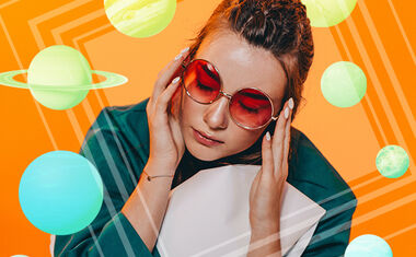 A woman wearing round sunglasses is seen against an orange background surrounded by colorful planets