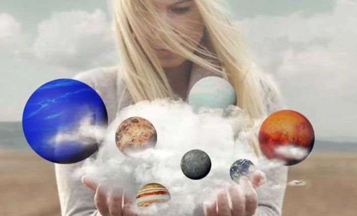 A woman looks over miniature planets in a cloud hovering above her hands.