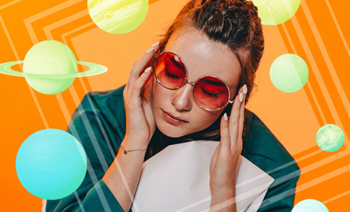A woman wearing round sunglasses is seen against an orange background surrounded by colorful planets