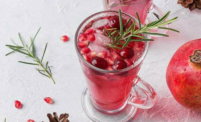 A winter cocktail with cranberries, pomegranate, and rosemary is shown on a white tablecloth.