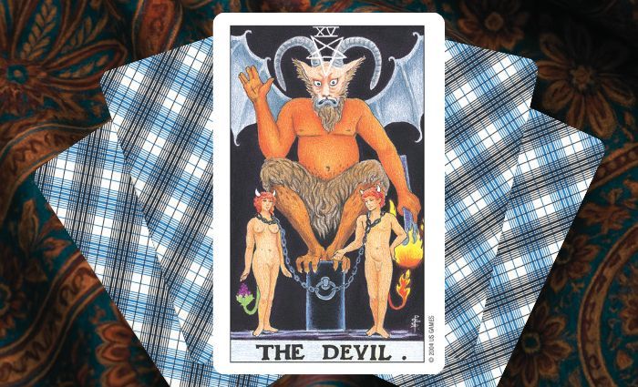 A classic Devil card rests on a floral tapestry.