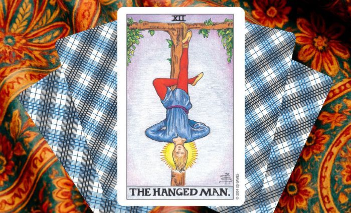 A classic Hanged Man card rests on a floral tapestry.