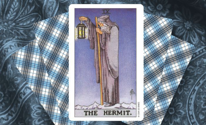 A classic Hermit card rests on a floral tapestry.