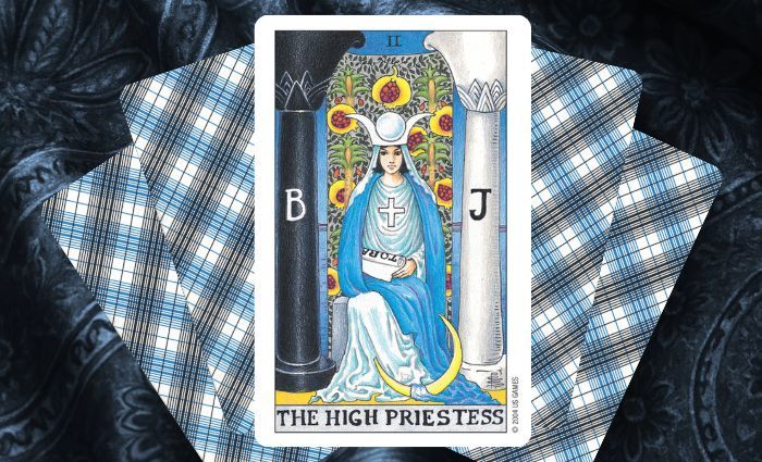 A classic High Priestess card rests on a floral tapestry.
