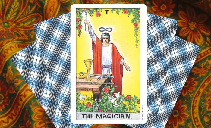 A classic Magician card rests on a floral tapestry.