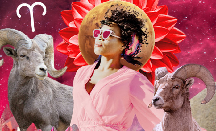 A woman in a pink robe and sunglasses stands with rams for the 2023 Aries yearly horoscope.